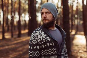 uma jovem homem com uma barba anda em dentro uma pinho floresta. retrato do uma brutal barbudo homem outono floresta foto