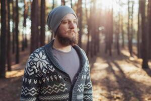 uma jovem homem com uma barba anda em dentro uma pinho floresta. retrato do uma brutal barbudo homem outono floresta foto