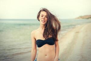 jovem sorridente mulher dentro Preto bikini em mar fundo foto