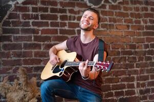 homem com acústico guitarra contra tijolo parede jogando música cantando canções apreciar vida médio tiro foto