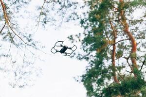 pequeno inteligente zangão quadrocopter vôo em branco céu e verde árvores foto