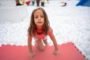 feliz pequeno menina jogando branco plástico bolas piscina dentro diversão parque. foto