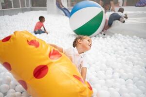 feliz pequeno menina jogando branco plástico bolas piscina dentro diversão parque. Parque infantil para crianças. foto