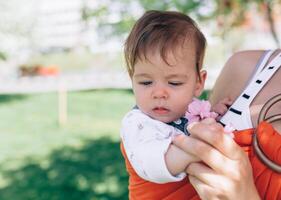 mãe levar uma infantil bebê dentro embrulho Funda dentro parque. primavera. conceito do natural parentalidade foto