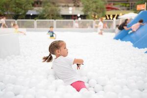 feliz pequeno menina jogando branco plástico bolas piscina dentro diversão parque. Parque infantil para crianças. foto