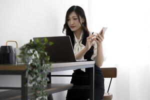 uma japonês mulher verificação Smartphone de controlo remoto trabalhos dentro a casa escritório foto