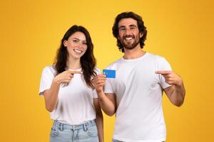 sorridente jovem casal dentro casual branco Camisetas, a mulher apontando às uma azul crédito cartão foto