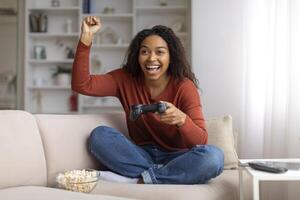 muito feliz jovem Preto mulher a comemorar ganhar enquanto jogando vídeo jogos às casa foto