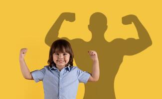 uma sorridente criança dentro uma azul camisa mostra fora músculos com uma Super heroi sombra dentro a fundo foto