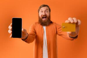 ruivo barbudo homem mostrando em branco Smartphone e crédito cartão, estúdio foto