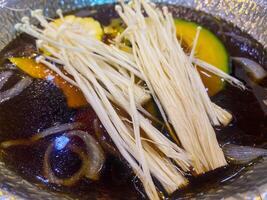 dourado agulha cogumelo e abóbora dentro Preto sopa, Sukiyaki foto