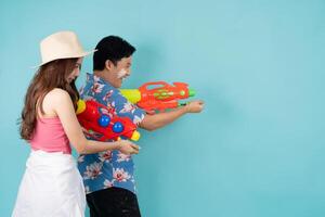 lado Visão do feliz ásia casal dentro verão roupas com água armas em azul fundo, songkran festival dentro Tailândia foto