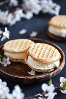 ai gerado baunilha gelo creme sanduíches com açucarado biscoitos em uma de madeira prato no meio florescendo galhos foto