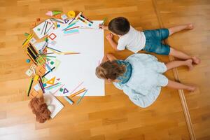 crianças desenhando em chão em papel. pré escola Garoto e menina jogar em chão com educacional brinquedos - blocos, trem, Ferrovia, avião. brinquedos para pré escola e Jardim da infância. crianças às casa ou creche. topo visualizar. foto