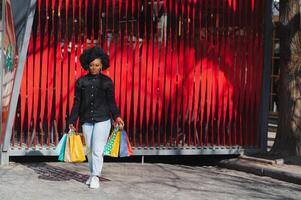 retrato lindo sorridente africano mulher com compras bolsas dentro cidade sobre vermelho fundo foto