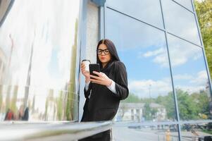 advogado empresária profissional caminhando ao ar livre falando em célula inteligente telefone bebendo café a partir de descartável papel copo. foto