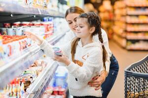 família dentro a supermercado. lindo jovem mãe e dela pequeno filha sorridente e comprando Comida. a conceito do saudável comendo. colheita foto