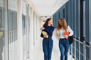 dois jovem mulheres com livro conversando enquanto em pé dentro Faculdade corredor. universidade alunos dentro corredor depois de a palestra. foto