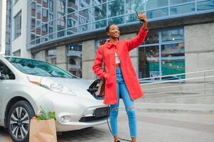africano americano menina cobrando eletro carro às a elétrico gás estação foto