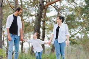 mãe, Papai e filho andar dentro a verde grama. feliz jovem família gastos Tempo junto, corrida fora, ir dentro natureza, em férias, ao ar livre. a conceito do família feriado. foto