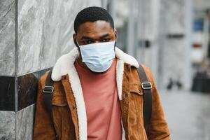 fechar-se retrato do uma à moda africano americano cara carrinhos sozinho dentro a rua dentro uma protetora mascarar em dele face. preventivo medidas. foto