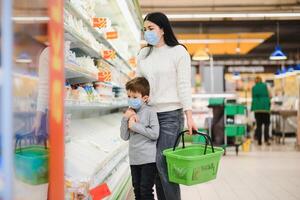 autêntico tiro do mãe e filho vestindo médico máscaras para proteger si mesmos a partir de doença enquanto compras para mercearias juntos dentro supermercado foto