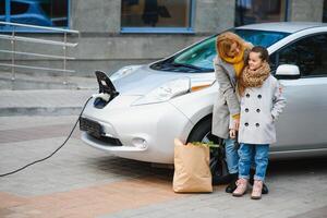 à moda mãe e filha carregar a elétrico carro, e gastar Tempo junto. foto