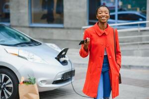africano americano menina cobrando eletro carro às a elétrico gás estação. foto