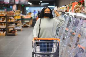 africano mulher vestindo descartável médico mascarar compras dentro supermercado durante coronavírus pandemia surto. epidemia Tempo foto