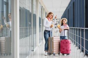 mulher com pequeno menina dentro internacional aeroporto. mãe com bebê esperando para seus voo. filha com dela mãe comendo bananas. viajando com crianças foto