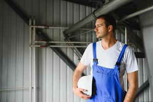 sorridente e feliz funcionário. industrial trabalhador dentro de casa dentro fábrica. jovem técnico com branco Difícil chapéu. foto