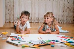 crianças desenhando em chão em papel. pré escola Garoto e menina jogar em chão com educacional brinquedos - blocos, trem, Ferrovia, avião. brinquedos para pré escola e Jardim da infância. crianças às casa ou creche foto