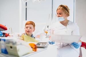 dentista vestindo mascarar. ruivo criança dentista vestindo mascarar examinando fofa Garoto foto