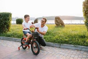 jovem e feliz pai ensina dele jovem filho para passeio uma bicicleta. a criança é feliz . pai assistindo filho. do pai dia foto