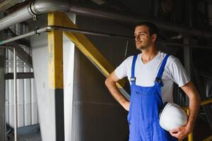 sorridente e feliz funcionário. industrial trabalhador dentro de casa dentro fábrica. jovem técnico com branco Difícil chapéu. foto