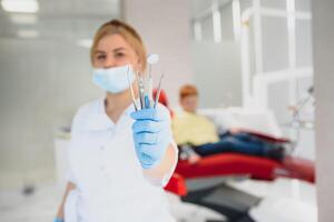 retrato do uma dentista segurando dental instrumentos dentro dele mãos dentro a clínica fechar-se foto
