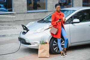 africano americano menina cobrando eletro carro às a elétrico gás estação. foto