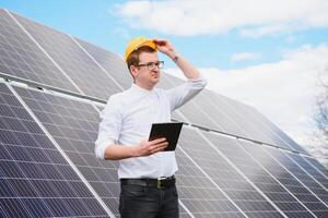 masculino engenheiro dentro capacete com tábua dentro mãos em pé perto solar painéis. conceito ecologia proteção. foto