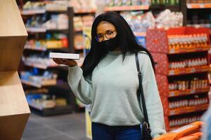 africano mulher vestindo descartável médico mascarar compras dentro supermercado durante coronavírus pandemia surto. epidemia Tempo foto