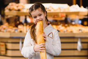 jovem e engraçado menina comendo baguetes dentro frente do a padaria loja foto