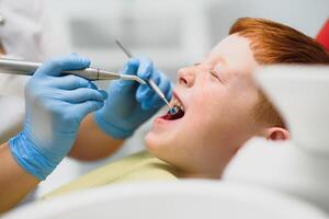 dentista vestindo mascarar. ruivo criança dentista vestindo mascarar examinando fofa Garoto foto