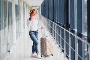 jovem mulher vestindo casual roupas é posando às aeroporto, aguarde saco e esperando perto bagagem dentro corredor avião partida. foto