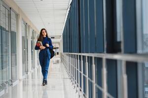 retrato do uma bonita fêmea aluna com livros e uma mochila dentro a universidade corredor foto