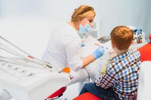 dentista vestindo mascarar. ruivo criança dentista vestindo mascarar examinando fofa Garoto foto