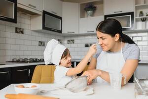 uma jovem e lindo mãe é preparando Comida às casa dentro a cozinha, ao longo com dela pequeno filho foto