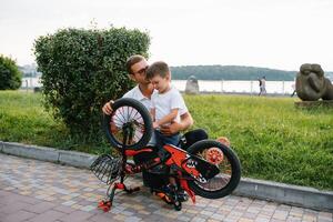 feliz pai e dele filho tendo Diversão juntos às a verde parque, fixação bicicleta junto. do pai dia. foto