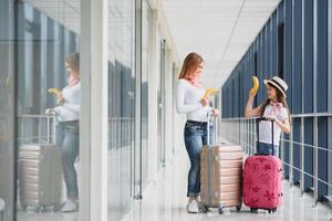 mulher com pequeno menina dentro internacional aeroporto. mãe com bebê esperando para seus voo. filha com dela mãe comendo bananas. viajando com crianças foto