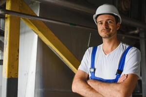 sorridente e feliz funcionário. industrial trabalhador dentro de casa dentro fábrica. jovem técnico com branco Difícil chapéu. foto