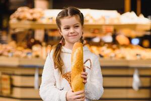 jovem e engraçado menina comendo baguetes dentro frente do a padaria loja foto