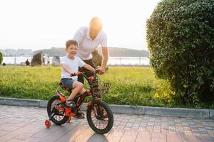 jovem e feliz pai ensina dele jovem filho para passeio uma bicicleta. a criança é feliz . pai assistindo filho. do pai dia foto